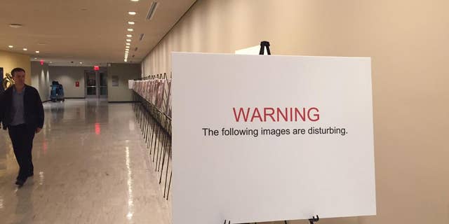 The sign warns of disturbing images as a man walks past a photo exhibit at United Nations headquarters, Tuesday, March 10, 2015. The graphic photo exhibit shows detainees who have died in Bashar Assad's prisons since the start of Syria's conflict. (AP Photo/Cara Anna)