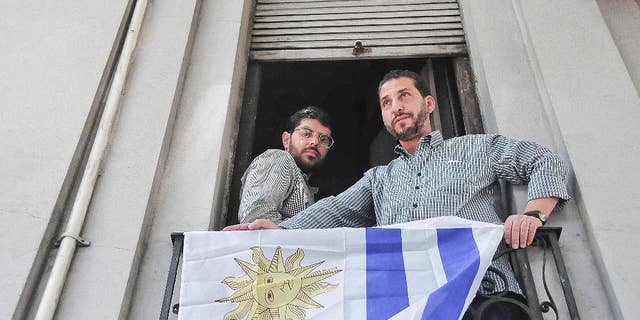 FILE - In this Dec. 11, 2014 file photo, Omar Abdelahdi Faraj, of Syria, left, and Adel bin Muhammad El Ouerghi, of Tunisia, look out at the press from their shared home's balcony decorated with Uruguay's flag in Montevideo, Uruguay. The two former Guantanamo Bay detainees who resettled in Uruguay are planning to tie the knot with women from the South American country. Imam Samir Selim said on Thursday, May 28, 2015 that he would officiate the ceremony. (Ines Guimaraens, Diario El Observador via AP, File) URUGUAY OUT - NOT FOR USE ON URUGUAY WEBSITES OR PUBLICATIONS - NO PUBLICAR EN URUGUAY - NO USAR EN PAGINAS WEBS O EN PAPEL EN URUGUAY