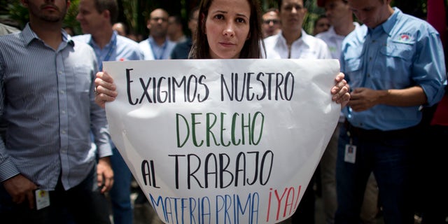 A Polar worker holds a sign that reads in Spanish: "We demand our right to work. Raw material now!" during a protest by workers who fear losing their jobs, outside company headquarters in Caracas, Venezuela, Friday, April 22, 2016. Polar, the largest producer of beer in the country, said Thursday the lack of imported raw materials could force them to stop producing beer starting April 29, when their current stock of malted barley would run out. (AP Photo/Ariana Cubillos)