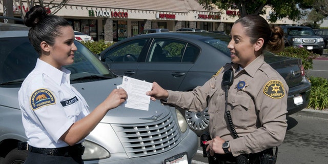 A deputy hands crime prevention tips to a Los Angeles County Sheriff's Department civilian volunteer, who are now allowed to issue parking violations to Malibu residents. (Courtesy: LASCD)