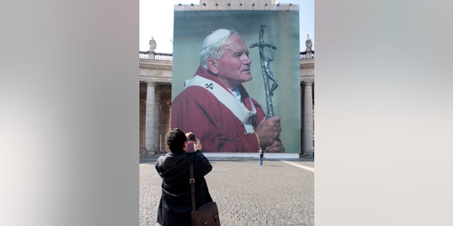 Faithful take a suovenir picture in front of a giant poster of late Pope John Paul II, in St. Peter's square, at the Vatican, April 28, 2011, days before John Paul's May 1 beatification. A prayer vigil on the Circus Maximus, an all-night prayer session in downtown Rome churches and the beatification Mass celebrated by Pope Benedict XVI top the agenda for the three-day event.