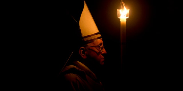March 30, 2013: Pope Francis holding a tall, lit, white candle, enters a darkened St. Peter's Basilica, at the Vatican to begin the Vatican's Easter vigil service.