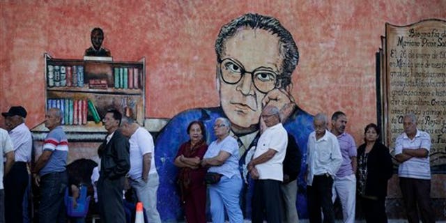 Residents in front of a wall with a painting depicting Venezuelan writer and diplomat Mariano Picon as they wait in line to enter a polling station to vote during municipal elections in Caracas, Venezuela, Sunday, Dec. 8, 2013. Venezuelans head to the polls to elect mayors and city councilors at a moment when the country's economic troubles have deepened, with inflation touching a two-decade high of 54 percent, and shortages of everything from toilet paper to milk spreading while the black market value of the currency plunges. (AP Photo/Ariana Cubillos)