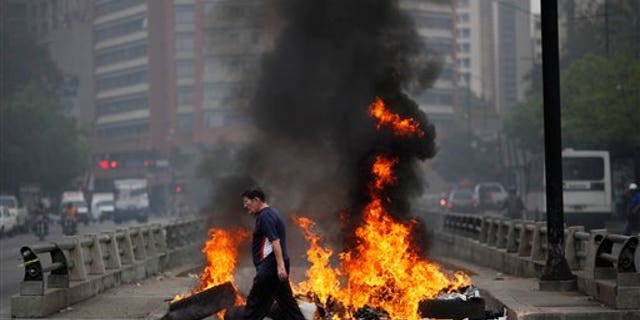 A pedestrian walks in front of a burning barricade blocking the highway in Chacao, Caracas, Venezuela, Monday, Feb. 24, 2014. Traffic has come to a halt in parts of the Venezuelan capital because of barricades set up by opposition protesters across major thoroughfares. The protests are part of a wave of anti-government demonstrations that have swept Venezuela since Feb. 12 and have resulted in at least 10 deaths. The protests in the capital Monday were peaceful. Police and National Guard troops stood by but did not act to remove the barricades despite the effect on the morning commute. (AP Photo/Rodrigo Abd)