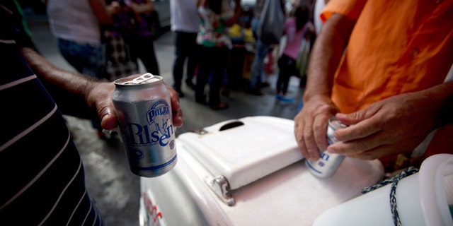 In this Tuesday, July 28, 2015 photo, customers open their cans of Polar beer outside a liquor store in downtown Caracas, Venezuela. Starting Monday Aug. 3, at least two of Polar's six beer plants is closing temporarily for lack of ingredients, affecting 25% of beer production in a country with one of the highest beer consumption rates in the world. Venezuela's President Nicolás Maduro blames food and goods shortages on an economic war waged by opposition aligned companies, while economists point to the country's price controls since 2003. (AP Photo/Fernando Llano)