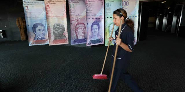 FILE - In this Feb. 10, 2015 file photo, a cleaning woman walks by replicas of Venezuela's currency bills, hung in a hallway at the Central bank office building in Caracas, Venezuela. The South American country debuted a new exchange system last week aimed at easing the country's economic crisis, and on Thursday, Feb. 19, 2015, Venezuelans got their first crack at trading local cash for paper dollars at banks and money exchangers. (AP Photo/Ariana Cubillos, File)