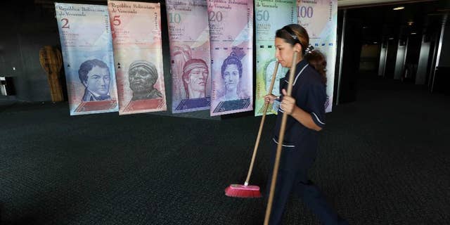 FILE - In this Feb. 10, 2015 file photo, a cleaning woman walks by replicas of Venezuela's currency bills, hung in a hallway at the Central bank office building in Caracas, Venezuela. The South American country debuted a new exchange system last week aimed at easing the country's economic crisis, and on Thursday, Feb. 19, 2015, Venezuelans got their first crack at trading local cash for paper dollars at banks and money exchangers. (AP Photo/Ariana Cubillos, File)