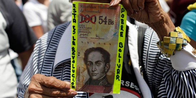 An anti-government protester holds up a fake Venezuelan banknote that reads in Spanish, "This is the revolution. Poor Bolivar."