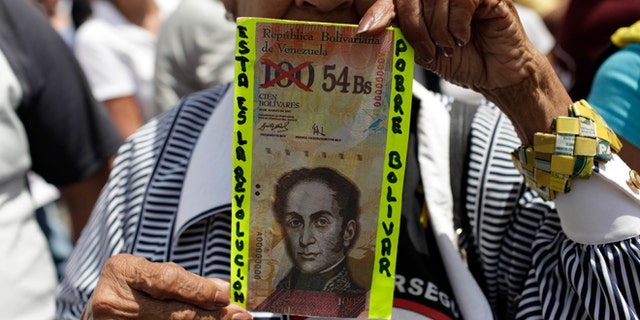An anti-government protester holds up a fake Venezuelan banknote that reads in Spanish, "This is the revolution. Poor Bolivar."