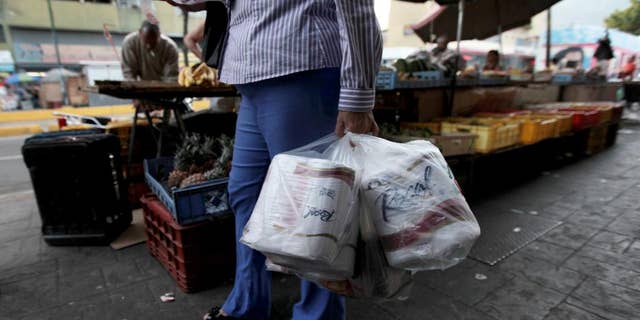 FILE- In this May 15, 2013 file photo, a woman who just bought toilet paper at a grocery store reads her receipt as she leaves the private store in Caracas, Venezuela. On Wednesday Sept. 10, 2014, Venezuela's President Nicolas Maduro reassured foreign creditors that his government will make good on a $4.5 billion foreign debt payment due next month. (AP Photo/Fernando Llano, File)
