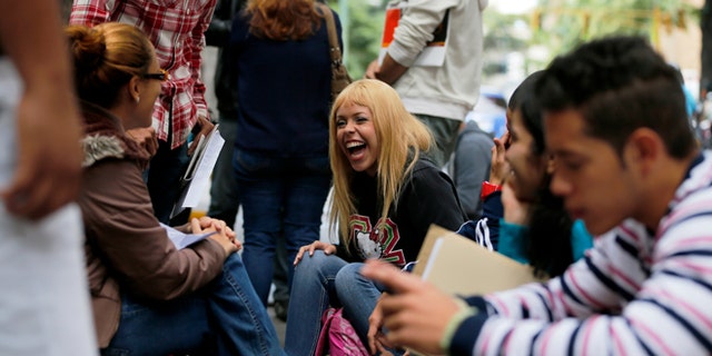 In this Jan. 28, 2014 photo, Daniela Rodriguez laughs with friends as she waits outside Ireland's consulate in Caracas, Venezuela. Venezuela's best and brightest are abandoning their homeland in droves. "I'll blindly go anywhere," said Rodriguez, who has been unable to find work as a journalist since graduating college in 2010, so instead works as a sales clerk at a clothing store. (AP Photo/Fernando Llano)