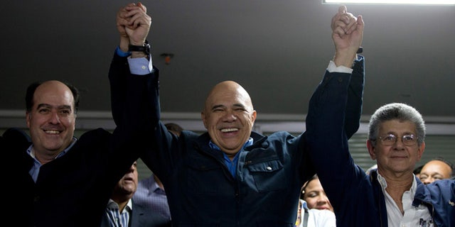 The General Secretary of Opposition coalition Jesus Torrealba, center, rise the arms of Venezuela National Assembly President candidates Julio Borges, left, and Henry Ramos Allup, right, in Caracas, Venezuela, Sunday, Jan. 3, 2016. Newly-elected opposition lawmakers voted in Ramos as National Assembly president Sunday. (AP Photo/Fernando Llano)