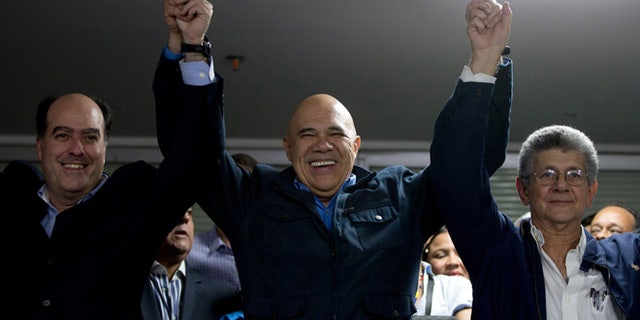 The General Secretary of Opposition coalition Jesus Torrealba, center, rise the arms of Venezuela National Assembly President candidates Julio Borges, left, and Henry Ramos Allup, right, in Caracas, Venezuela, Sunday, Jan. 3, 2016. Newly-elected opposition lawmakers voted in Ramos as National Assembly president Sunday. (AP Photo/Fernando Llano)