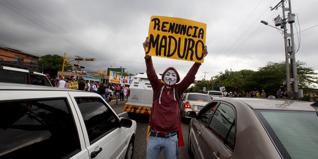 FILE - In this Jan. 23, 2015, file photo, a demonstrator wearing a Guy Fawkes mask displays a poster that reads in Spanish "Maduro Resign" during a protest in San Cristobal, Venezuela. A crop of new candidates who raged in the streets against Venezuelas socialist administration last spring, are now putting their faith in the ballot box as a means to force President Nicolas Maduro from power. (AP Photo/Fernando Llano, File)