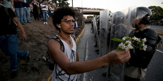 A student offers a small bouquet of flowers to police officers during a protest in Caracas, Venezuela, Friday, Feb. 14, 2014. Students are protesting the Wednesday killings of two university students who were shot in different incidents following an anti-government protest that demanded the release of student protesters who had been arrested in various parts of the country.(AP Photo/Alejandro Cegarra)