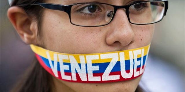An anti-government demonstrator stands with a tri-colored ribbon covering her mouth that reads "Venezuela" during a protest in front of an office of the Organization of American States, OAS, in Caracas, Venezuela, Friday, March 21, 2014. Opposition lawmaker Maria Corina Machado is scheduled to speak before the OAS council in a closed-door session Friday in Washington D.C., presenting the situation in her country (AP Photo/Esteban Felix)