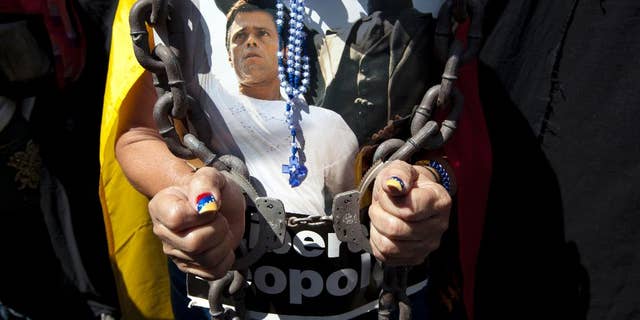 FILE - In this Feb. 18, 2015 file photo, a woman wearing handcuffs, chains and a rosary holds a poster of jailed opposition leader Leopoldo Lopez at an event marking the one year anniversary of his arrest and imprisonment in Caracas, Venezuela. Prosecutor Franklin Nieves, who reportedly is now seeking asylum in the United States, said in a video posted Monday, Oct. 26, 2015 on the Venezuelan news website La Patilla that superiors in the prosecutor's office had given him orders to have Lopez arrested days before the Caracas protest - and the alleged crime - took place. Lopez was convicted in September 2015 of inciting violence during a 2014 anti-government protest in Caracas and received the maximum sentence, about 14 years. (AP Photo/Ariana Cubillos, File)