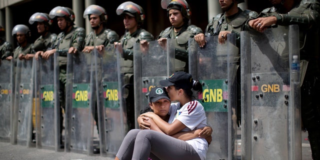 Women embrace as they sit in front of a line of National Bolivarian Guard outside the Palace of Justice court in Caracas, Venezuela, Wednesday, Feb. 19, 2014. Following a dramatic surrender and a night in jail, Venezuelan opposition leader Leopoldo Lopez was due in court Wednesday to learn what charges he may face for allegedly provoking violence during protests against the socialist government in the divided nation. (AP Photo/Rodrigo Abd)