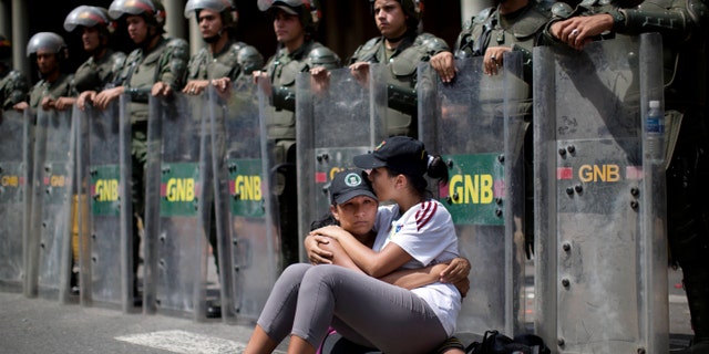 Women embrace as they sit in front of a line of National Bolivarian Guard outside the Palace of Justice court in Caracas, Venezuela, Wednesday, Feb. 19, 2014. Following a dramatic surrender and a night in jail, Venezuelan opposition leader Leopoldo Lopez was due in court Wednesday to learn what charges he may face for allegedly provoking violence during protests against the socialist government in the divided nation. (AP Photo/Rodrigo Abd)