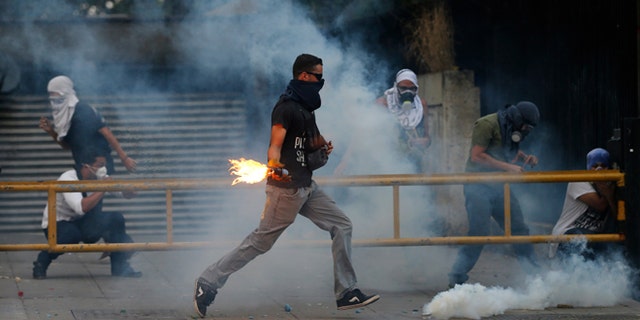 A demonstrator runs to throw a molotov bomb against Bolivarian National Police officers during clashes in Caracas, Venezuela, Thursday, March 6, 2014. A National Guardsman and a civilian were killed Thursday in a clash between residents of a Caracas neighborhood and armed men who tried to remove a barricade, Venezuelan officials said. (AP Photo/Fernando Llano)