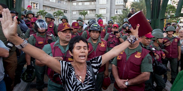 A woman prays with a bible in her hand, in front of Bolivarian National Guard officers during an anti-government protest in Plaza Altamira, Caracas, Venezuela, Tuesday, March 18, 2014. Protesters blocked the streets only when traffic lights turned red under the watchful gaze of the National Guard. Security forces have taken control of the plaza that has been at the heart of anti-government protests that have shaken Venezuela for a month. (AP Photo/Esteban Felix)