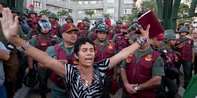 A woman prays with a bible in her hand, in front of Bolivarian National Guard officers during an anti-government protest in Plaza Altamira, Caracas, Venezuela, Tuesday, March 18, 2014. Protesters blocked the streets only when traffic lights turned red under the watchful gaze of the National Guard. Security forces have taken control of the plaza that has been at the heart of anti-government protests that have shaken Venezuela for a month. (AP Photo/Esteban Felix)