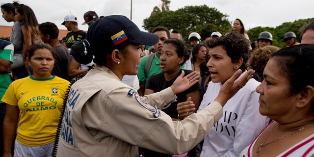 A police officer talks to an angry crowd during a protest for food at the Catia neighborhood in Caracas, Venezuela, Tuesday, June 14, 2016. Tensions rose after customers waited in line for hours and their frustration turned into a street protest. (AP Photo/Fernando Llano)