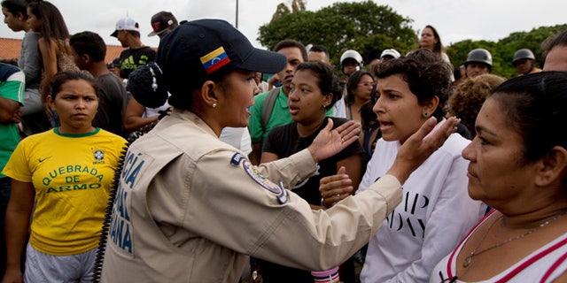 A police officer talks to an angry crowd during a protest for food at the Catia neighborhood in Caracas, Venezuela, Tuesday, June 14, 2016. Tensions rose after customers waited in line for hours and their frustration turned into a street protest. (AP Photo/Fernando Llano)