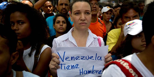 An opposition members holds a handwritten message that that reads in Spanish; "Venezuela is hungry," during a protest outside the court offices of the Chacao municipality, in Caracas, Venezuela, Wednesday, May 25, 2016. Opposition members held a demonstration to demand authorities hold a recall referendum on cutting short Nicolas Maduro's presidency. (AP Photo/Fernando Llano)