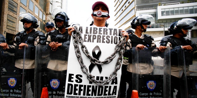 Feb. 11, 2014: A woman with her mouth covered stands before a line of National Bolivarian Police preventing protesters from reaching the national intelligence agency in Caracas, Venezuela.