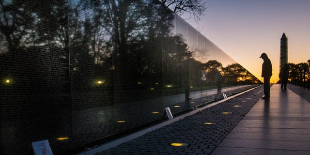 A visitor at the Vietnam War Memorial in Washington passes early in the morning on Veterans Day, Monday, to look at the names inscribed on the wall.