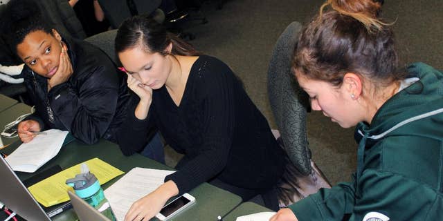 In this March 1, 2015 photo released by Joe Grimm, Michigan State University students Tiara Jones, from left, Madeline Carino and Lia Kamana work on a new book “100 Questions and Answers About Veterans” in East Lansing, Mich. The new book, researched and written by a Michigan State journalism class with assistance from former servicemen and women, is aimed at clearing up myths and misunderstandings held by some civilians. (AP Photo/Joe Grimm)