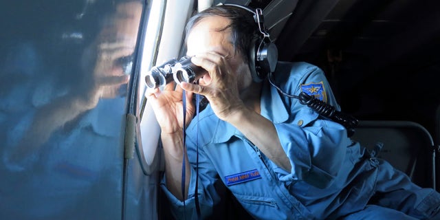 Vietnamese Air Force Col. Pham Minh Tuan uses binoculars on board a flying aircraft during a mission to search for the missing Malaysia Airlines flight MH370 in the Gulf of Thailand over the location where Chinese satellite images showed possible debris from the missing Malaysian jetliner, Thursday, March 13, 2014. (AP Photo)