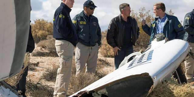 In this Nov. 1, 2014, photo provided by the National Transportation Safety Board, Virgin Galactic pilot Todd Ericson, right, talks with NTSB Acting Chairman Christopher A. Hart, second from left, at the SpaceShipTwo accident site with investigators in Mojave, Calif. The cause of Friday's crash of Virgin Galactic's SpaceShipTwo has not been determined, but investigators found the "feathering" system, which rotates the tail to create drag, was activated before the craft reached the appropriate speed, National Transportation Safety Board Acting Chairman Christopher Hart said. (AP Photo/NTSB)