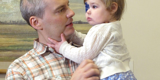 Brian Wilson, of Scotch Plains, N.J. holds his 2-year-old daughter Vivian as they prepare to deliver boxes of letters to Gov. Chris Christie's office in Trenton, N.J., on Thursday, Aug. 1, 2013. (AP Photo/Geoff Mulvihill)