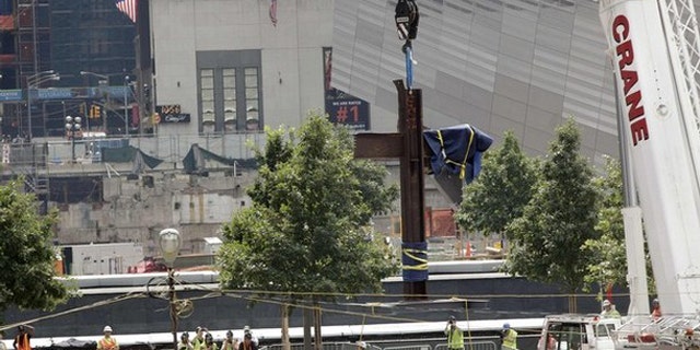 July 23: The World Trade Center Cross, made of intersecting steel beams found in the rubble of buildings destroyed in the September 11 attacks on the World Trade Center, is raised by a crane before being transported and lowered into an opening in the World Trade Center site below ground level where it will become part of the permanent installation exhibit in the 9/11 Memorial and Museum.