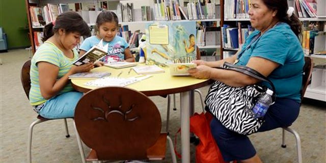 In this Friday, July 19, 2013 photo, Maria Lopez, right, reads in the city library alongside daughters Emily, 9, at left, and Esmeralda, 7, in Watsonville, Calif. In the bricked plaza, strolling musicians wearing glitzy cowboy outfits blast a mariachi song, while Spanish-speaking shoppers bustle between farm stands choosing tasty cactus leaves and fresh chiles. Welcome to an increasingly typical town in California, a state where Hispanics become the largest ethnic group this summer. As the Golden State becomes less and less white, communities are becoming more segregated, not less. (AP Photo/Marcio Jose Sanchez)
