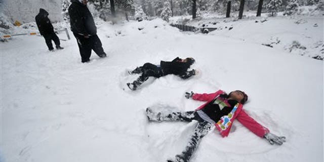 Darius Gomez, 9, center, and Amanda Lopez, 7, both from Palmdale, Calif, make snow angels together during their visit to Wrightwood, Calif, on Friday, Nov 22, 2013. (AP Photo/The Victor Valley Daily Press, David Pardo)