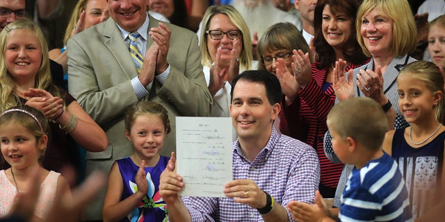 July 12, 2015: Wisconsin Governor Scott Walker displays a signed 2015-2017 state budget during a ceremony on the production floor of Valveworks USA in Waukesha, Wis. (John Hart/Wisconsin State Journal via AP)
