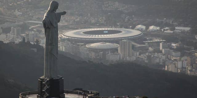 In this May 13, 2014, photo,This aerial view shot through an airplane window shows the Maracana stadium behind the Christ the Redeemer statue in Rio de Janeiro, Brazil. As opening day for the World Cup approaches, people continue to stage protests, some about the billions of dollars spent on the World Cup at a time of social hardship, but soccer is still a unifying force. The international soccer tournament will be the first in the South American nation since 1950. (AP Photo/Felipe Dana, File)