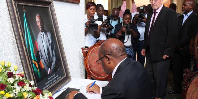 Acting Zambian president Guy Scott, second from right, watches over as eductaion minister John Phiri, foreground, signs a book of condolences in Lusaka, Friday, Oct. 31, 2014. Scott has taken over as acting president after President Michael Sata, in framed photo left, passed away in a London hospital last Sunday night. Sata's body will be returned to Lusaka, Saturday, with a state funeral planed for Nov. 11, 2014. (AP PhotoMoses Mwape)