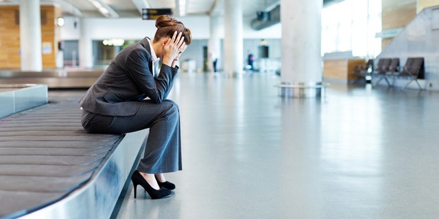 Businesswoman sits on an airport luggage conveyor belt with her head in her hands. Horizontal shot.