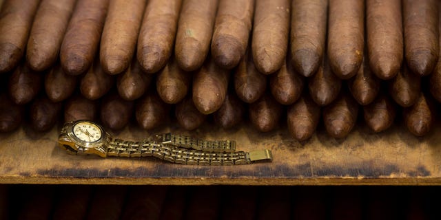 Sur cette photo du 26 février 2015, la montre d'un employé se trouve à côté d'une pile de cigares à l'usine de cigares Corona à La Havane, Cuba.  Les fabricants de cigares cubains se lèchent les nouvelles règles américaines qui permettent à davantage d'Américains de se rendre sur l'île et de rapporter légalement jusqu'à 100 dollars en stogies prisées pour la première fois depuis des décennies. 