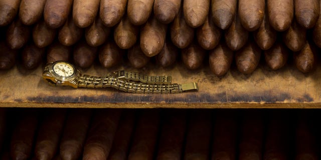 In this Feb. 26, 2015 photo, an employee's watch sits next to a stack of cigars at the Corona cigar factory in Havana, Cuba. Cuban cigar makers are licking their chops over new U.S. rules that let more Americans travel to the island and legally bring back as much as $100 worth in prized stogies for the first time in decades.