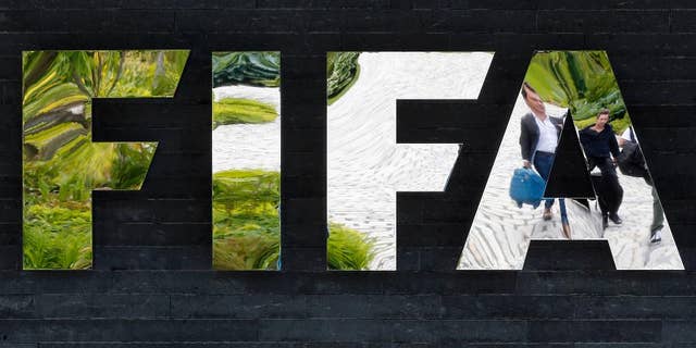 FILE - In this May 27, 2015, file photo, two persons are reflected in the FIFA logo at the FIFA headquarters in Zurich, Switzerland. Swiss authorities said Thursday, July 16, 2015, that one of the seven FIFA officials arrested in Zurich as part of a U.S. corruption probe was extradited to the United States they day before. Switzerland's Federal Office of Justice didn't identify the FIFA official. (AP Photo/Michael Probst, File)