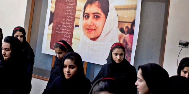 In this Thursday, Nov. 15, 2012 photo, Pakistani girls gather under a poster of Malala Yousufzai in her old school in Mingora, Swat Valley, Pakistan. The giant poster of her that once emblazoned the wall of the assembly hall has been removed. The school made no plans to recognize the anniversary of Malala's shooting by Taliban, teachers and students are afraid. (AP Photo/Anja Niedringhaus)