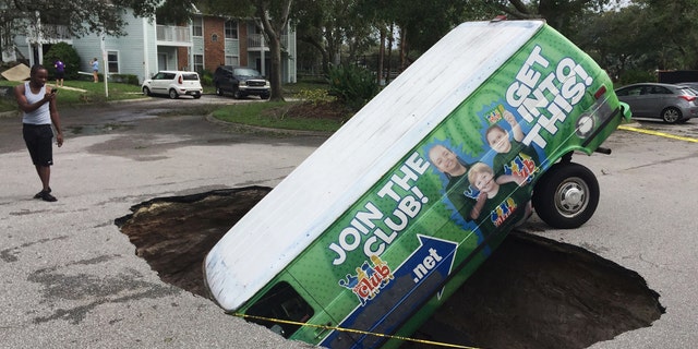 A boy photographs a van in a sinkhole in Winter Springs, Fla., Monday, Sept. 11, 2017, after Hurricane Irma. (Joe Burbank/Orlando Sentinel via AP)
