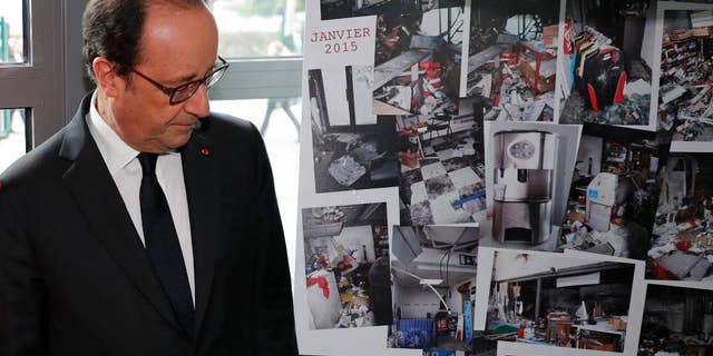 French President Francois Hollande walks past photographs of the devastated printing plant after the attack, as the plant reopens Thursday.