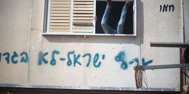 A settler jumps into a trailer in Amona outpost in the West Bank, Wednesday, Feb. 1, 2017. Israeli forces have begun evacuating a controversial settlement Amona, which is the largest of about 100 unauthorized outposts erected in the West Bank without permission but generally tolerated by the Israeli government. The writing reads: "Eretz Israel we did not betray ". (AP Photo/Ariel Schalit)
