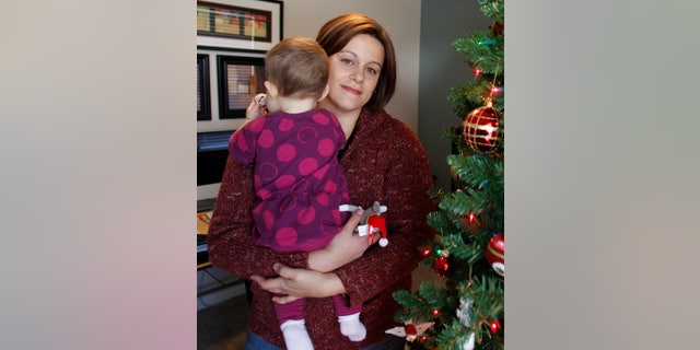 FILE - This is a Dec. 2011 file photo, Christa Dias holds her 11-month-old daughter in her Withamsville, Ohio home. Dias, a teacher who was fired from Catholic schools in 2010 after becoming pregnant through artificial insemination, testified Wednesday,May 29, 2013 in her federal lawsuit against the Roman Catholic Archdiocese of Cincinnati and two schools. She told jurors that she didn't know the procedure violated church doctrine or that she could be fired for it. (AP Photo/The Cincinnati Enquirer, Gary Landers, File) MANDATORY CREDIT; NO SALES